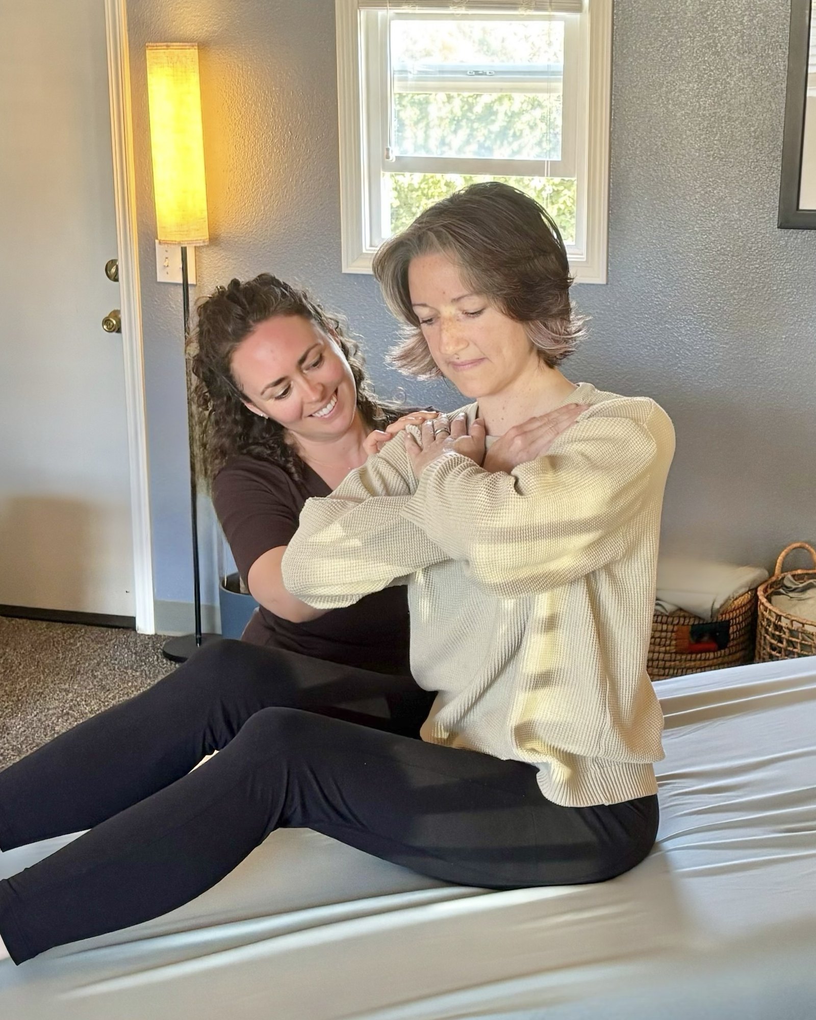 Juliet smiling as she works on a seated client's shoulders